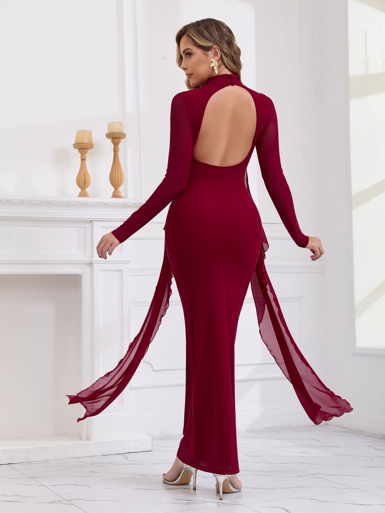 Back view of a woman in a long red formal dress with an open back and sheer sleeves.