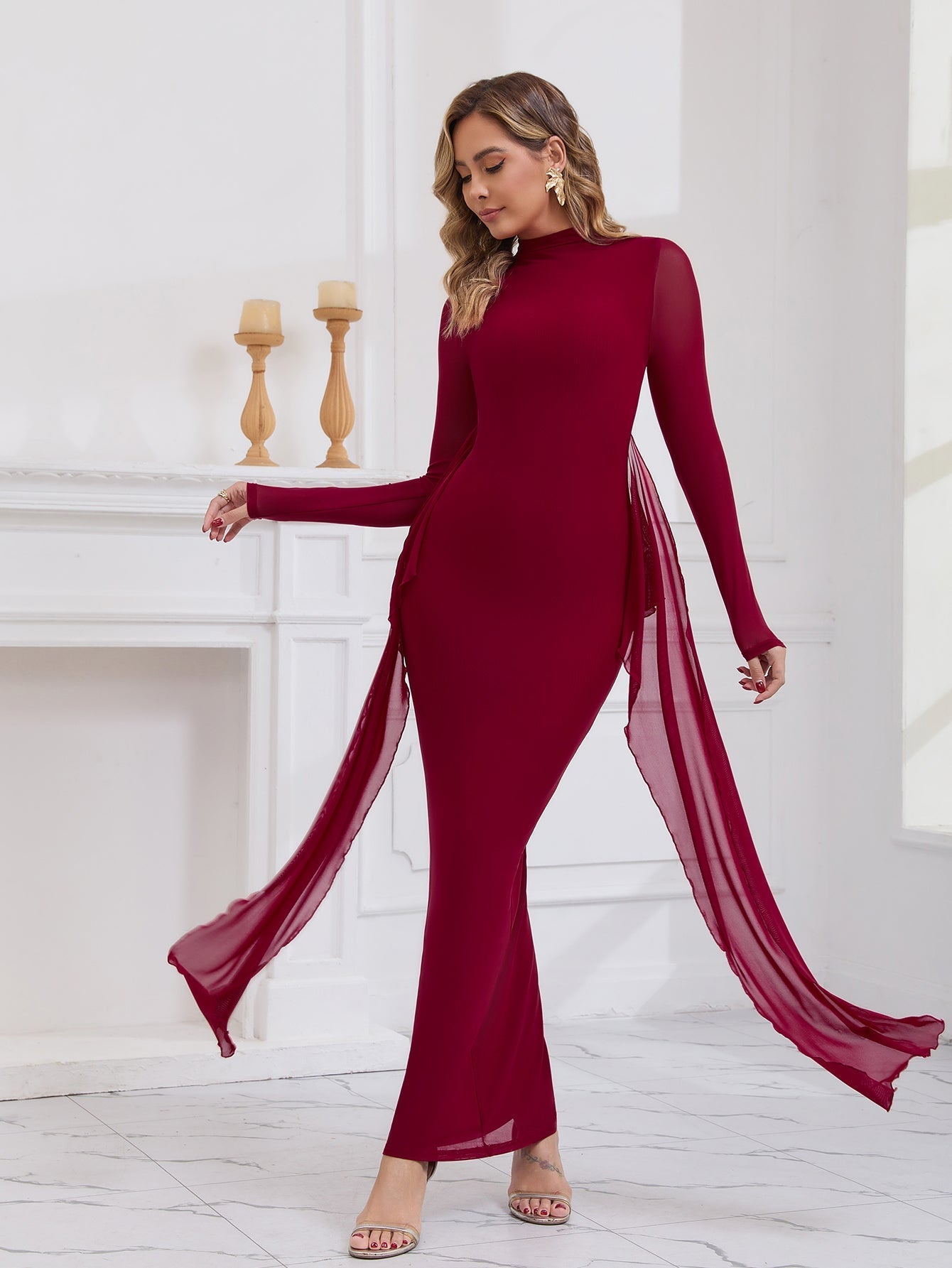 Woman in a long red formal dress with draping chiffon panels, posing with her hand on her hip.