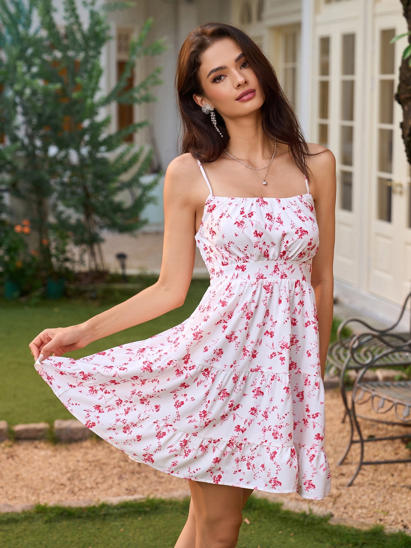 Woman in a white floral print dress with red flowers, lifting the hem of the tiered skirt.