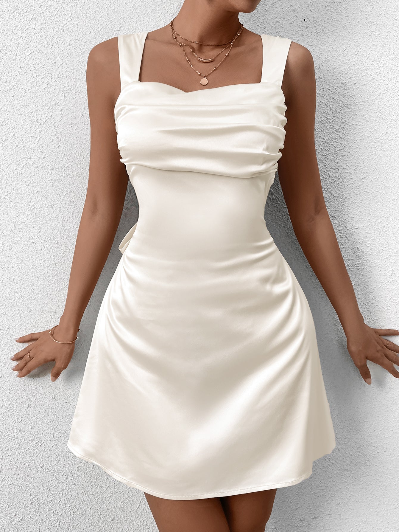 Model wearing a cream satin ruched mini dress with a square neckline and adjustable straps.