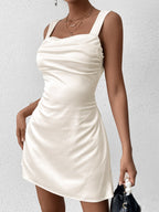Woman in a cream satin mini dress with a tie-back detail.