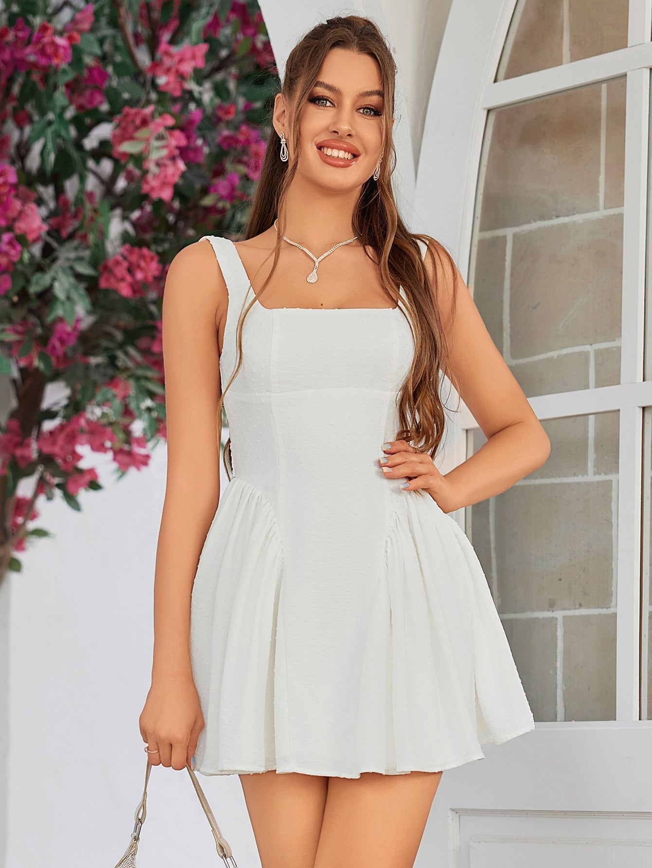 Front view of a woman in a white sleeveless mini dress with a square neckline and pleated skirt, smiling.