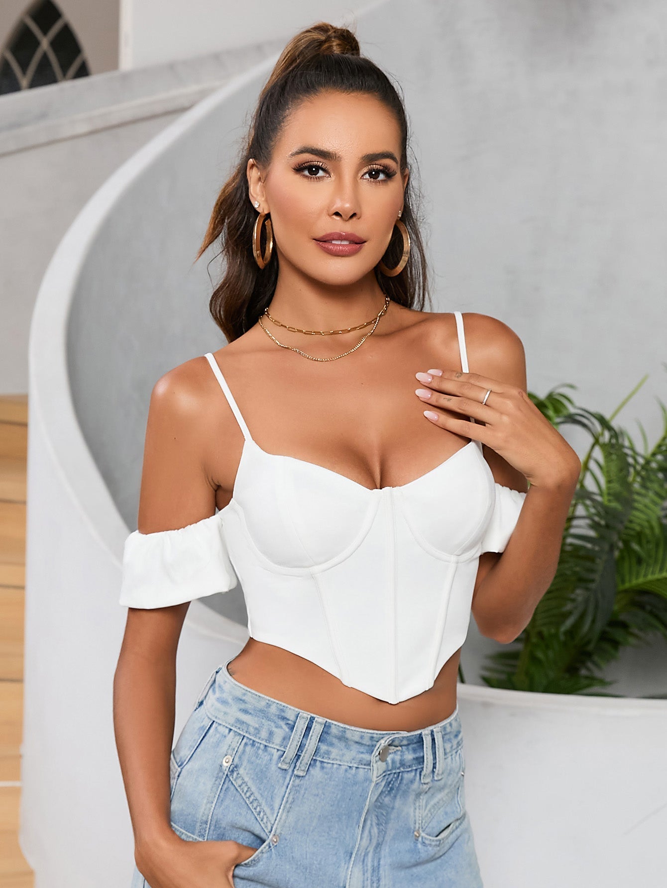 Woman wearing a white off-the-shoulder corset crop top with spaghetti straps and ruffled sleeves, paired with light wash denim jeans.