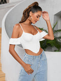 Woman in a white off-the-shoulder corset crop top and denim jeans, posing with her hand on her forehead.