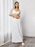 Woman standing in front of a white curtain wearing a white lace crop top and maxi skirt