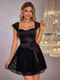 Woman in a black satin and lace A-line dress with sweetheart neckline and cap sleeves, standing in front of a chandelier.