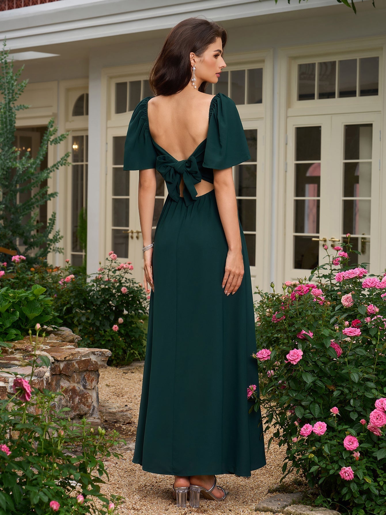 Back view of a woman in a dark green maxi dress with an open back and bow detail