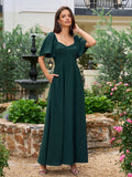 Woman in a dark green maxi dress with flutter sleeves and sweetheart neckline standing in a garden