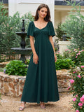 Woman in a dark green formal dress posing in an outdoor setting with a fountain