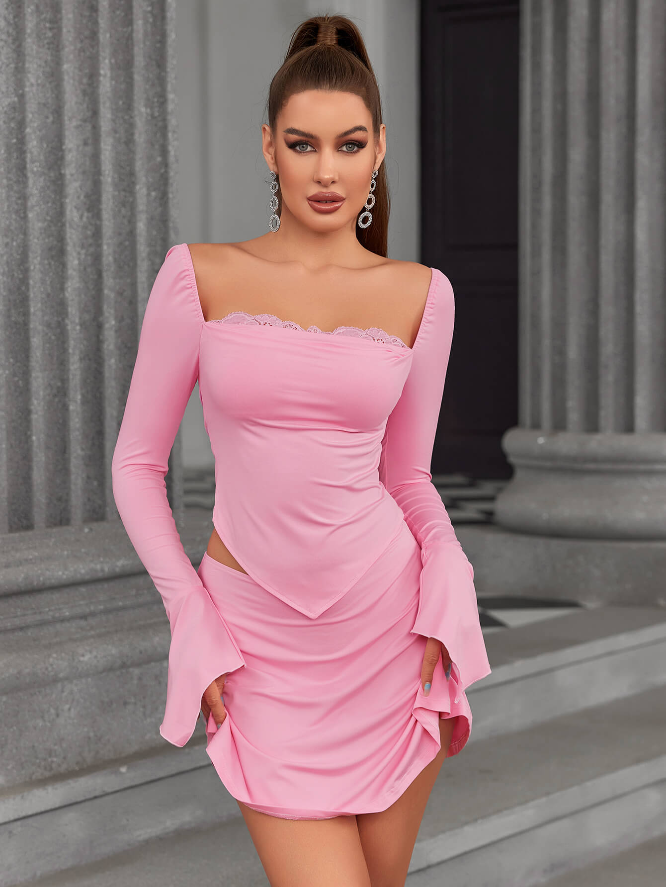 Full body shot of a woman in a pink long-sleeve top and skirt set with flared cuffs.