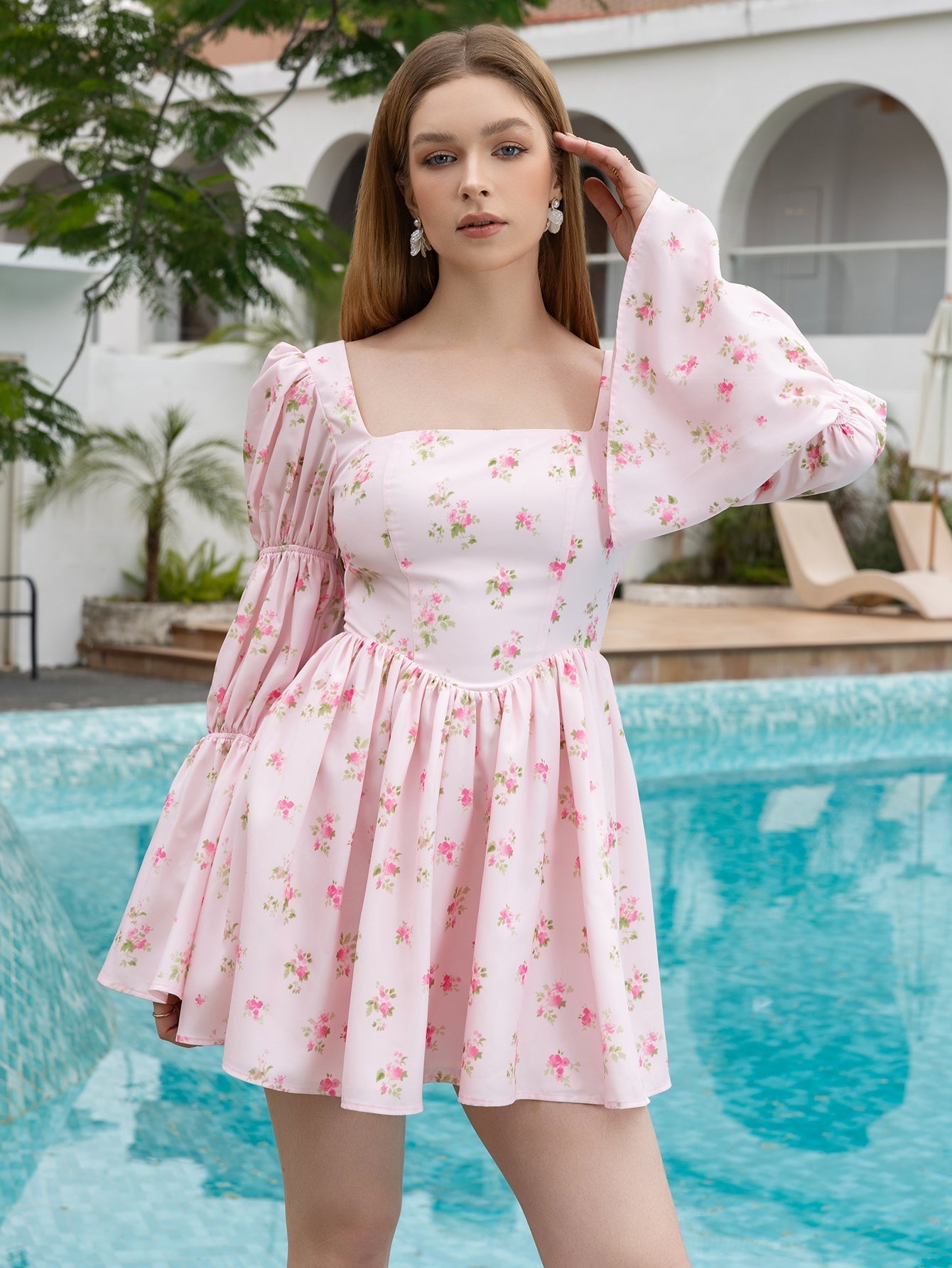 Woman posing in a pink floral puff sleeve mini dress by a pool