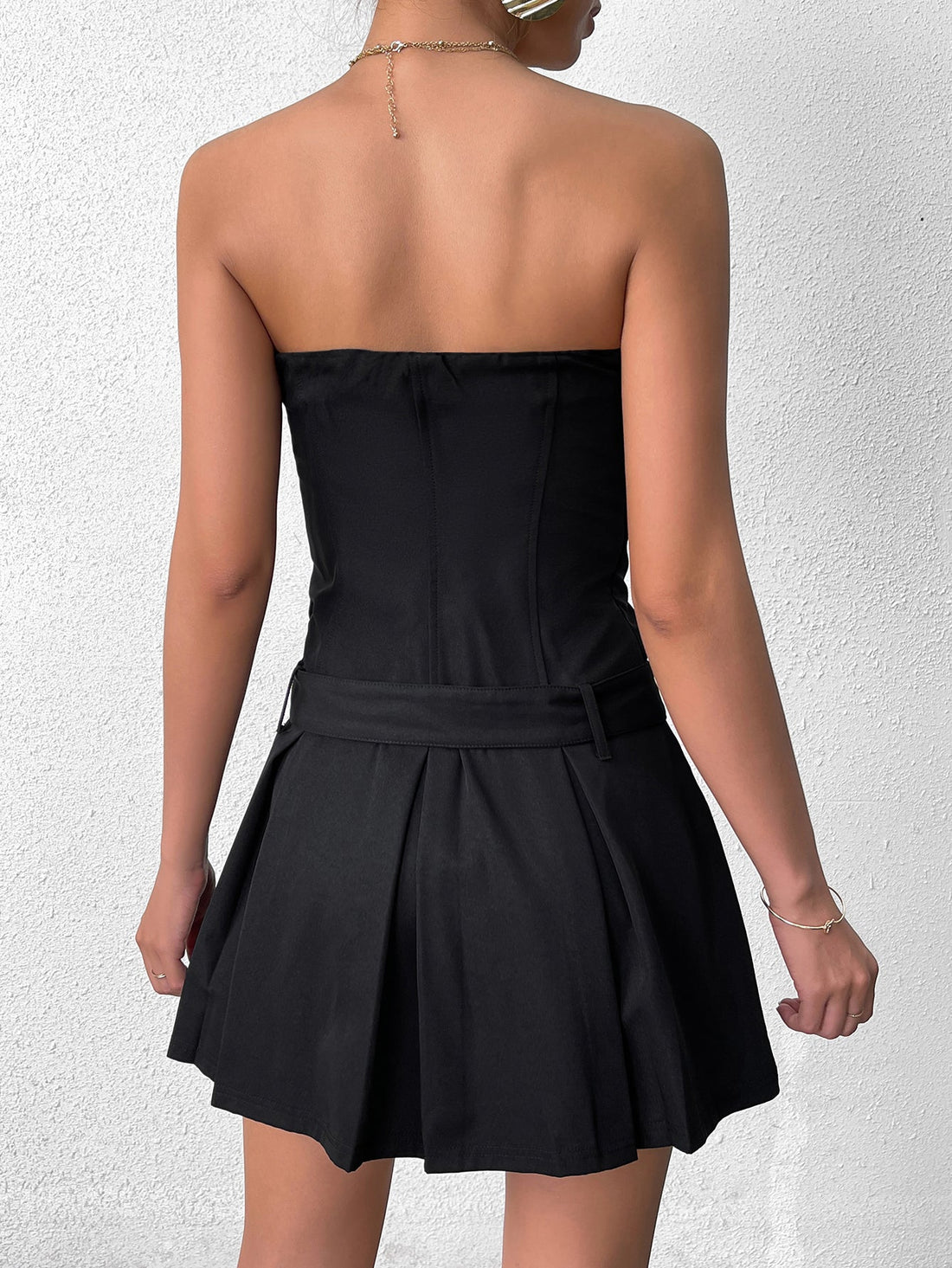 Woman wearing a black strapless dress with a buckle belt and pleated skirt