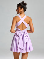Back view of a woman in a lavender smocked mini dress with criss-cross straps and a large bow
