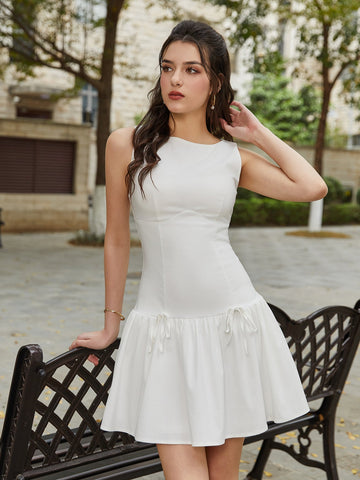 Woman wearing a white sleeveless A-line dress with a round neckline and a tiered skirt with tie details.