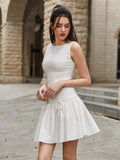 Woman looking down while wearing a white sleeveless A-line dress with a round neckline and tiered skirt.