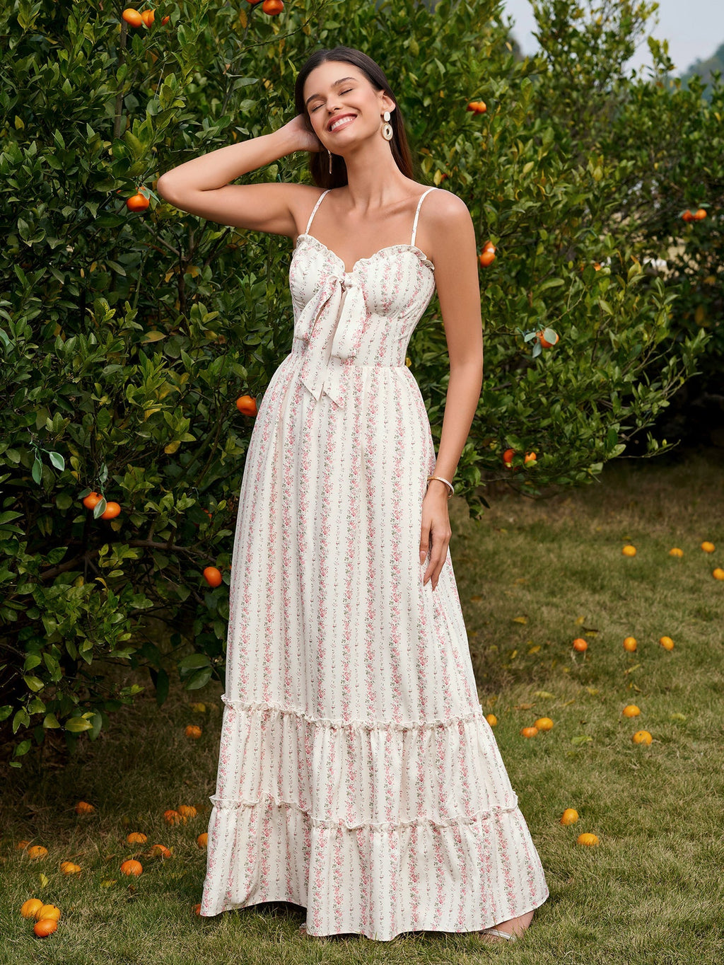 Woman in a floral print maxi dress with spaghetti straps and a tie-front bodice posing with her hand on her head.