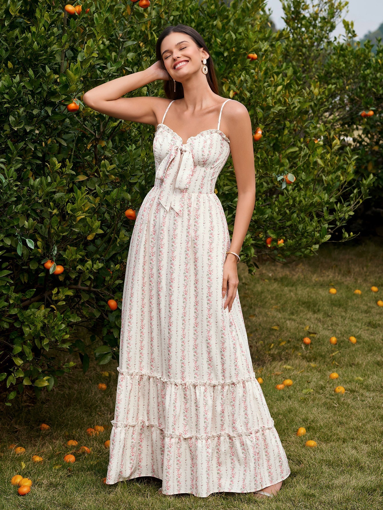 Woman in a floral print maxi dress with spaghetti straps and a tie-front bodice posing with her hand on her head.
