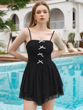 Woman wearing a black mini dress with white bow details and spaghetti straps, standing by a pool.