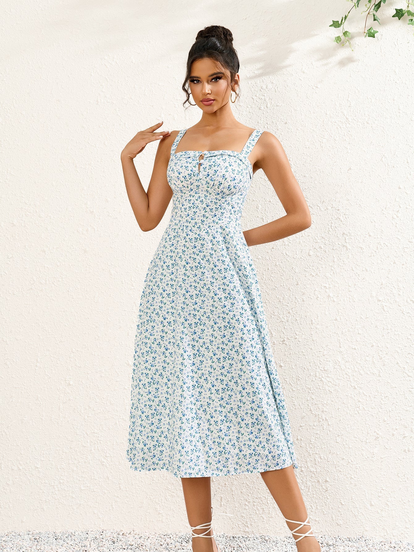 Woman wearing a white midi dress with a blue floral print, square neckline, and tie detail.