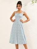 Woman with hands on hips wearing a white midi dress with a blue floral print and tie detail at the bust.