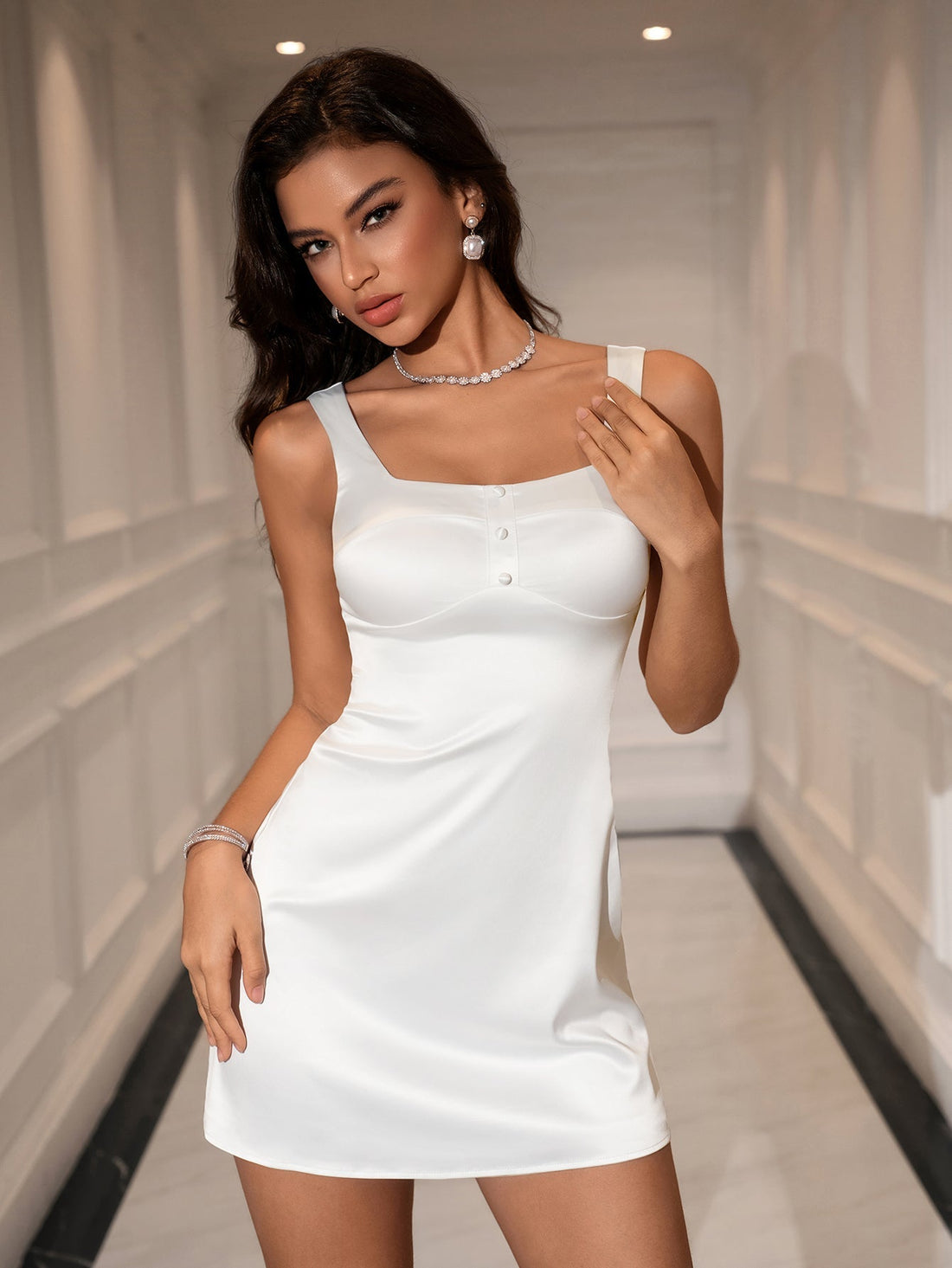 Woman wearing a white satin sleeveless square neck dress with button accents and a zipper closure.