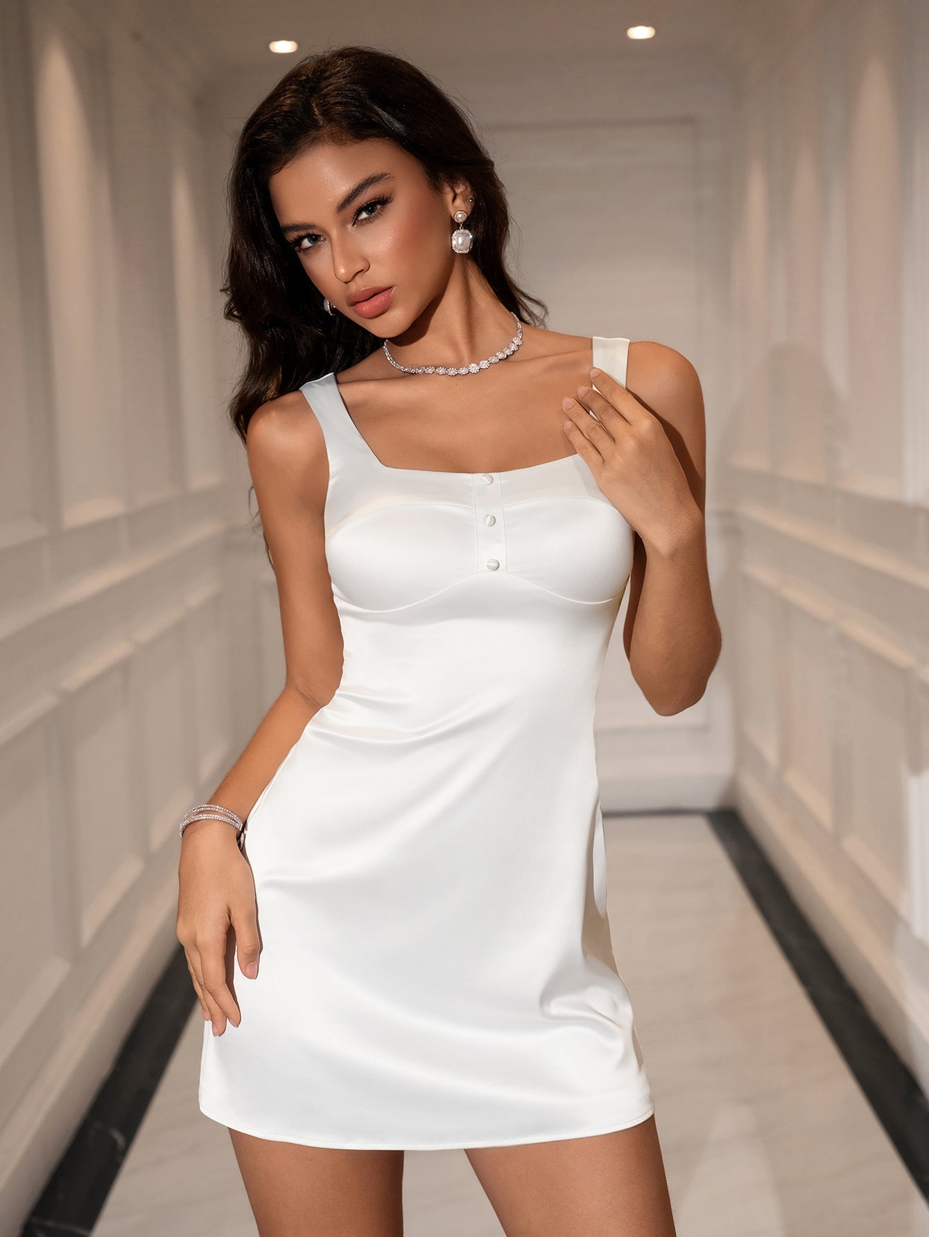Woman wearing a white satin sleeveless square neck dress with button accents and a zipper closure.