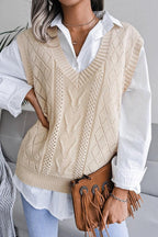 Front view of a woman wearing a beige cable knit V-neck sleeveless sweater vest over a white collared shirt, holding a brown fringed clutch.