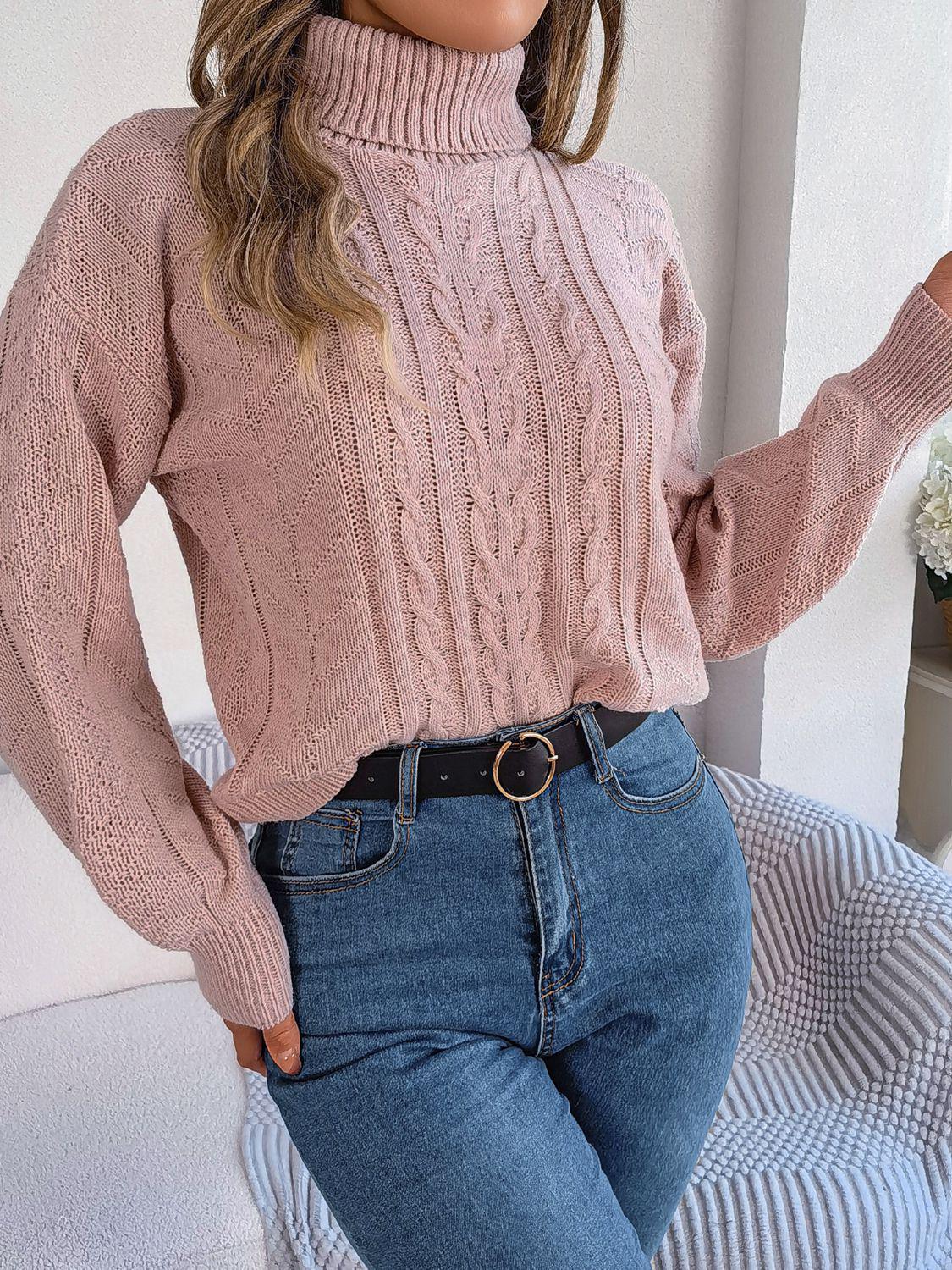 Woman wearing a pink cable knit turtleneck sweater and blue jeans with a black belt
