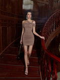 Full body shot of a woman in a taupe ruched off-the-shoulder bodycon mini dress on a wooden staircase.