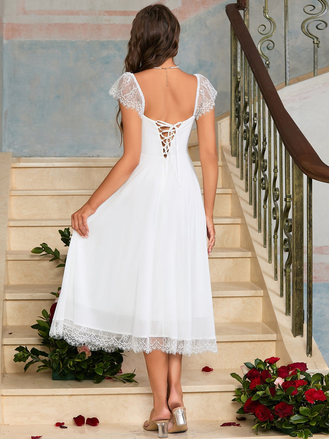 Woman in a black satin fit and flare midi dress with spaghetti straps and white lace trim.