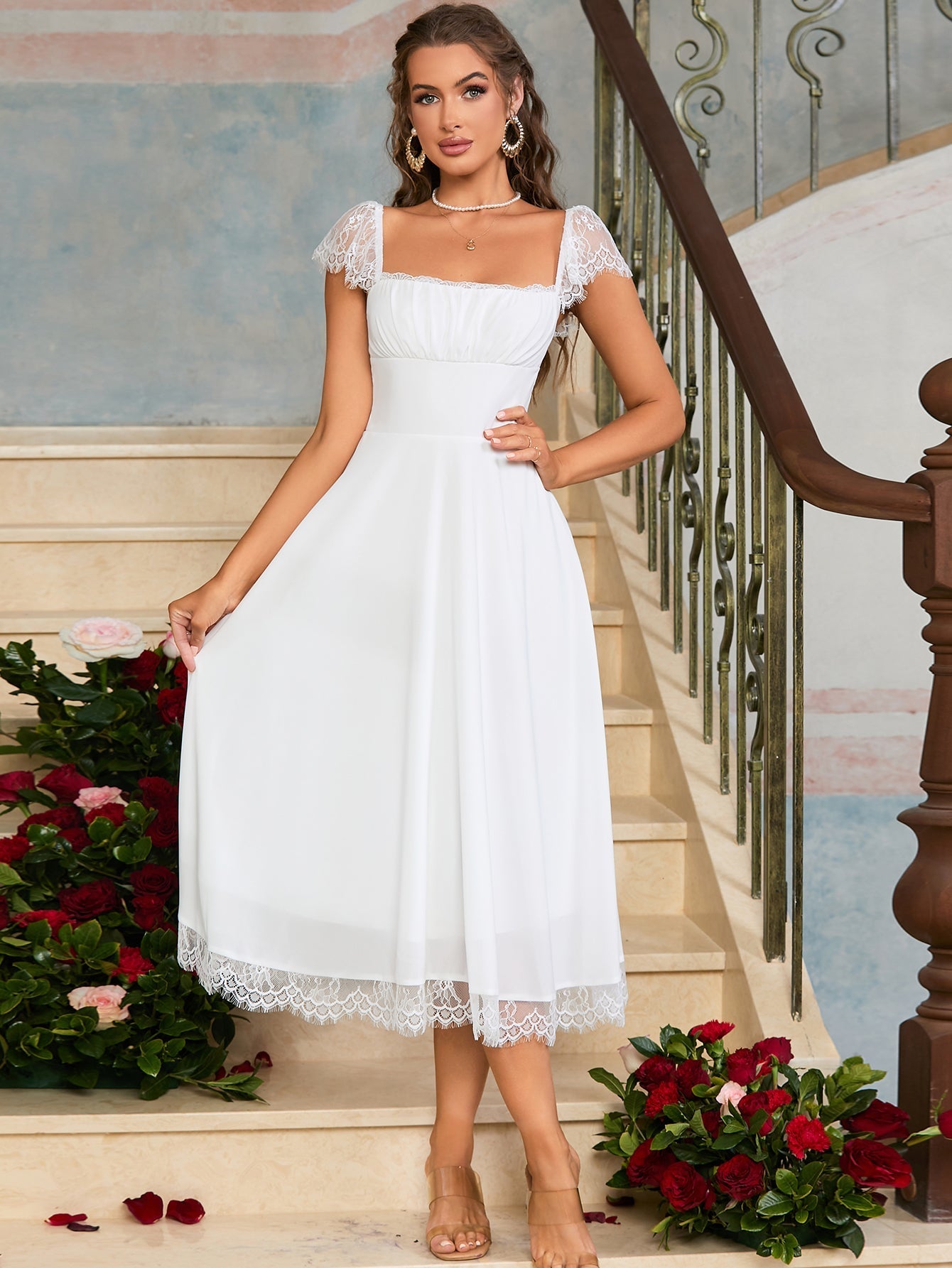 Front view of a woman in a black satin fit and flare midi dress with spaghetti straps and white lace trim, holding a silver clutch.