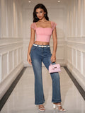Full body shot of a woman in a pink crop top, blue jeans, and holding a pink handbag