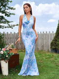 Woman in a blue and white abstract print mermaid gown with a cowl neckline and halter tie, posing outdoors.