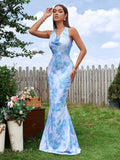 Woman standing in a garden wearing a blue and white abstract print mermaid gown with a cowl neckline and halter straps.