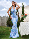Woman posing in a garden wearing a blue and white abstract print mermaid gown with a cowl neckline.