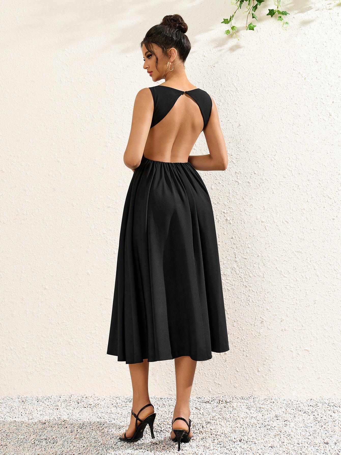back view of a woman in a sleeveless black crepe midi dress with an open back detail