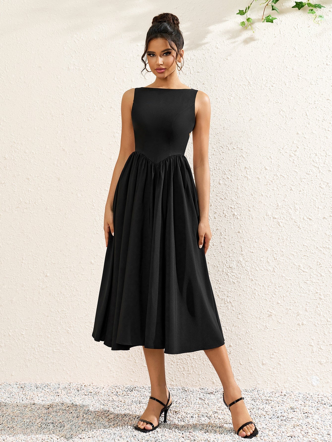 full body shot of a woman wearing a black crepe midi dress with a boat neckline and flared skirt