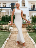 Woman holding a white handbag and wearing a white sleeveless ribbed knit mermaid gown.