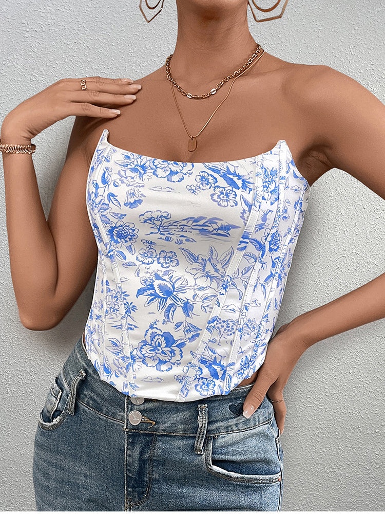 Front view of a woman wearing a white and blue floral print corset top with gold necklaces.