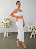 Woman posing in a white strapless cropped top and a white midi skirt with a side slit, with hands on hips.
