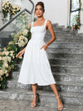 Woman with hands in pockets wearing a white sleeveless midi dress with adjustable straps, standing on stairs.