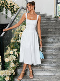 Woman holding a blue handbag, wearing a white sleeveless midi dress with lace trim on the neckline, standing on stairs.