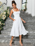 Woman in a white sleeveless midi dress with pockets, showing the fit and flare silhouette while standing on stairs.