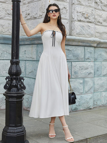 Woman wearing a white strapless midi dress with black tie detail, leaning against a lamppost