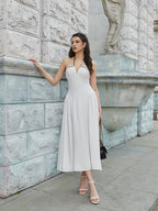 Woman posing in a white halter midi dress with contrast trim, leaning against a stone wall
