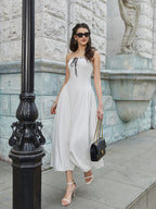 Woman walking in a white strapless midi dress with black tie detail, carrying a black handbag