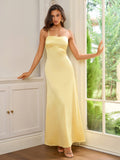Woman leaning against a doorframe in a yellow satin gown with spaghetti straps.