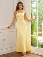 Woman leaning against a doorframe in a yellow satin gown with spaghetti straps.