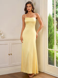 Woman wearing a long yellow satin dress with spaghetti straps and a square neckline, standing indoors.