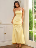 Woman holding the hem of a flowing yellow satin dress with spaghetti straps.